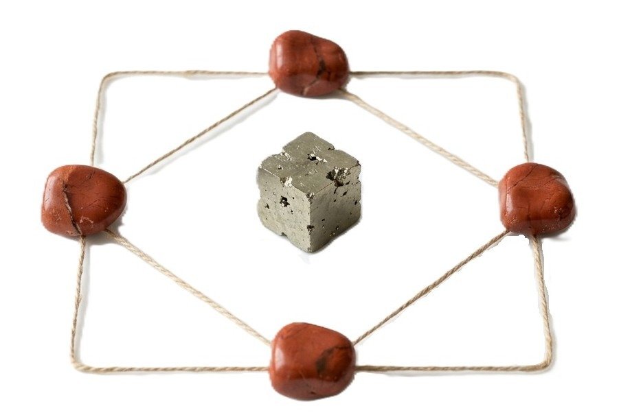 Sacred geometry crystal grid featuring four polished red jasper stones and a natural pyrite cube center connected by twine lines on a white background